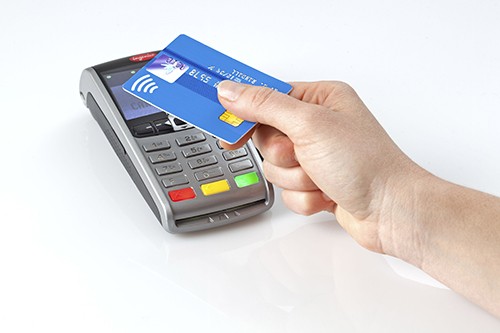 A hand paying a card machine via contactless with a blue credit card.