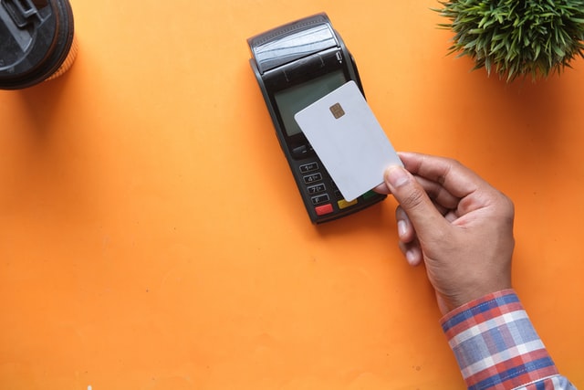 A hand paying a card machine via contactless with a white bank card.