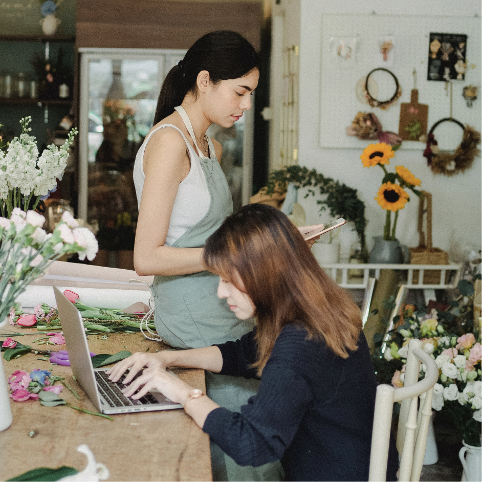 a woman working on a computer at a cafe while a waitress holds a card reader to take payment