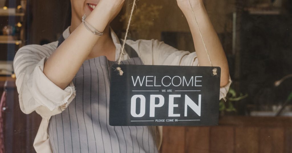 a woman starting a business in Ireland, hanging a sign that reads "welcome, open"