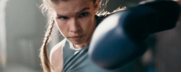 A lady throwing a punch with her left hand, she is wearing black boxing gloves.