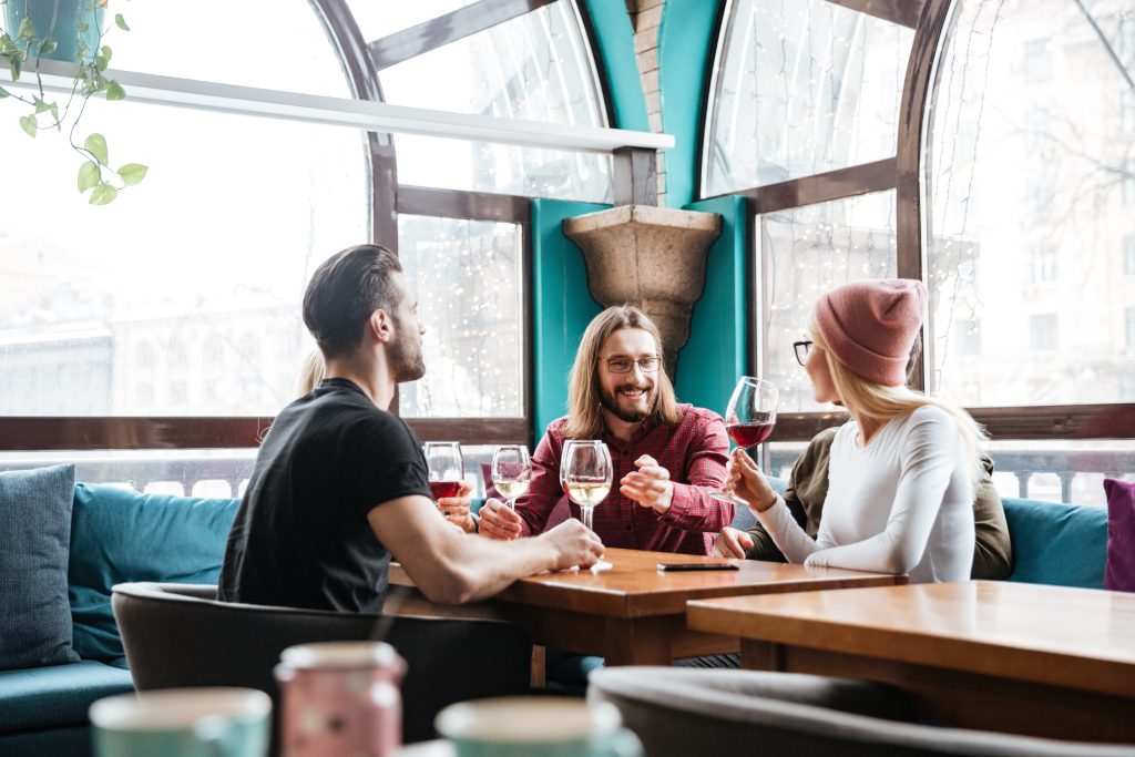 Three international tourists enjoying wine at an Irish restaurant while making payments with multi-currency card options