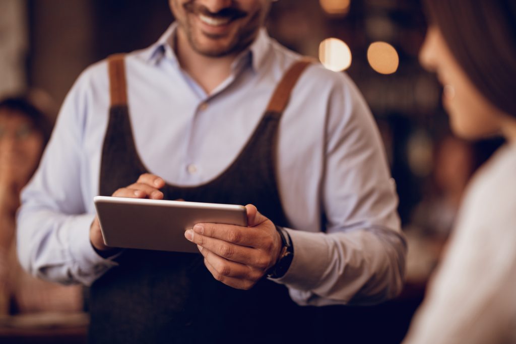 Irish pub staff member using payment terminal touchpad while serving customer demonstrating payment training Ireland